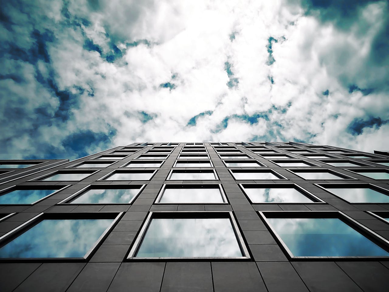 Low angle of a modern skyscraper reflecting clouds in its glass windows with a dramatic sky.